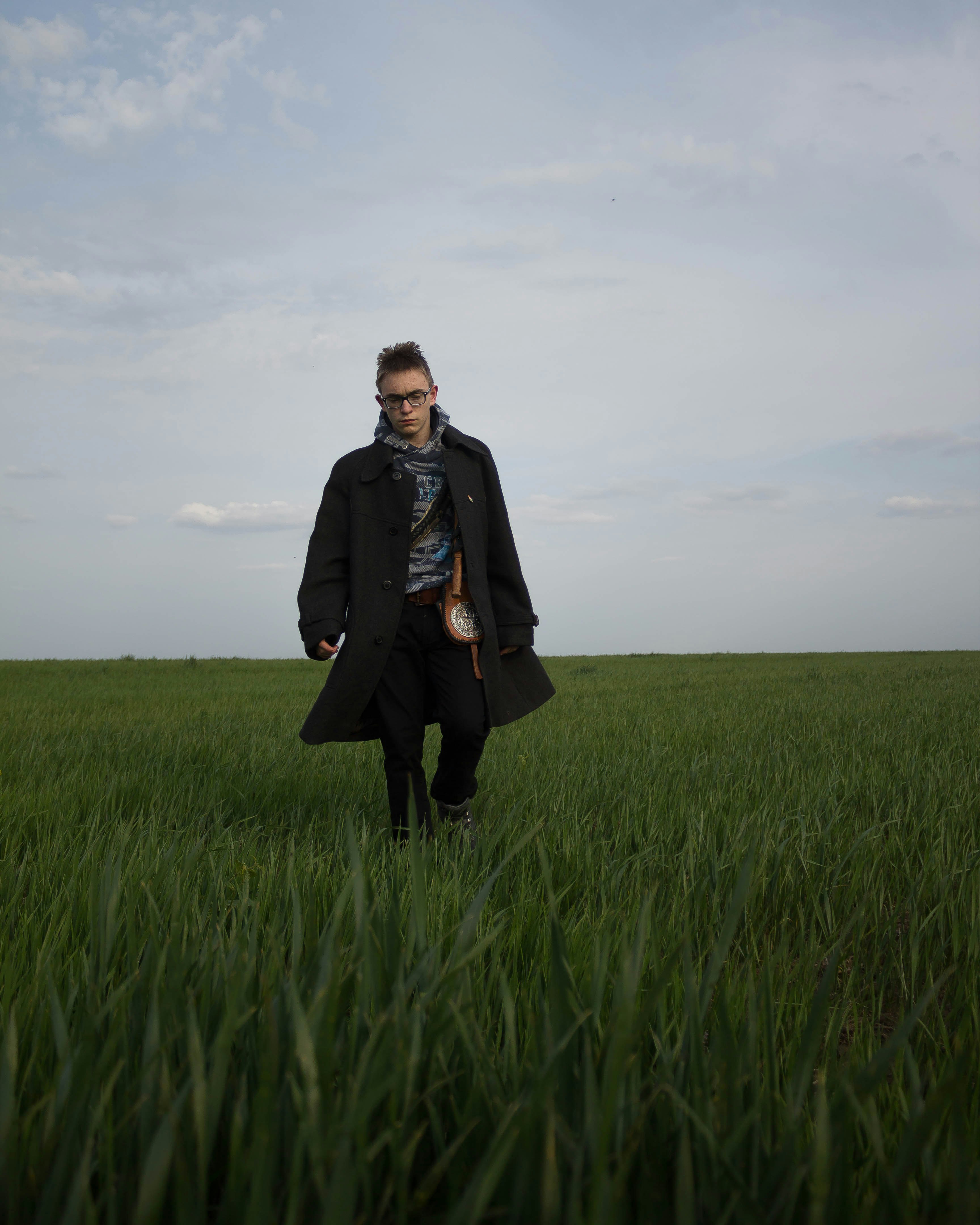 woman in black coat standing on green grass field under gray cloudy sky during daytime